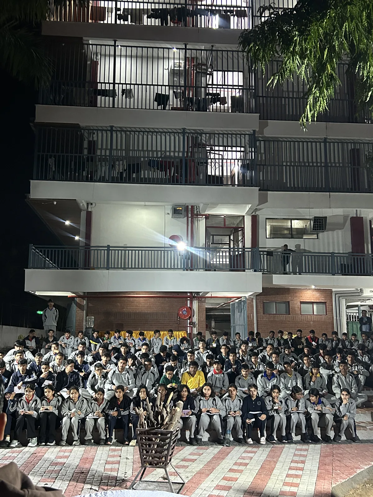 Students seated in the courtyard for an evening gathering by the hostel block