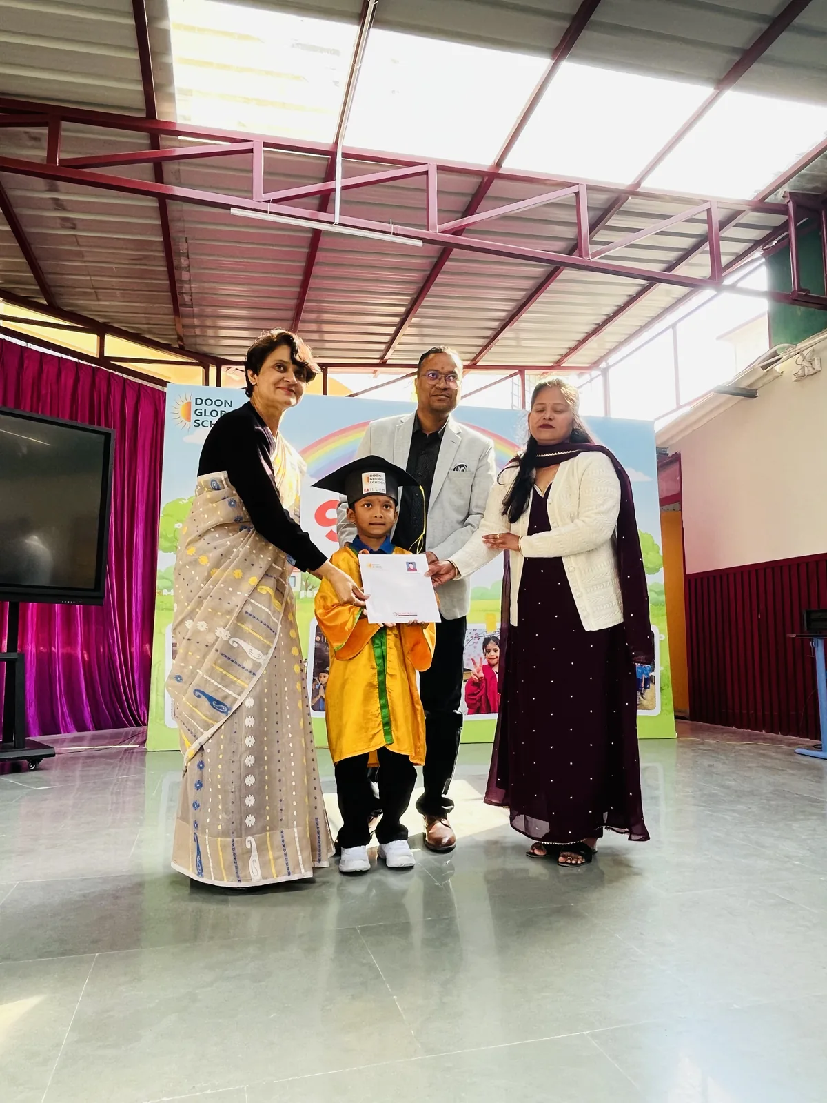 A young graduate in cap and gown receiving a certificate from staff