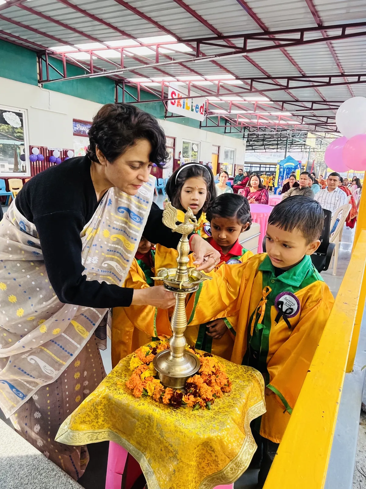A teacher helping a young student light the ceremonial lamp