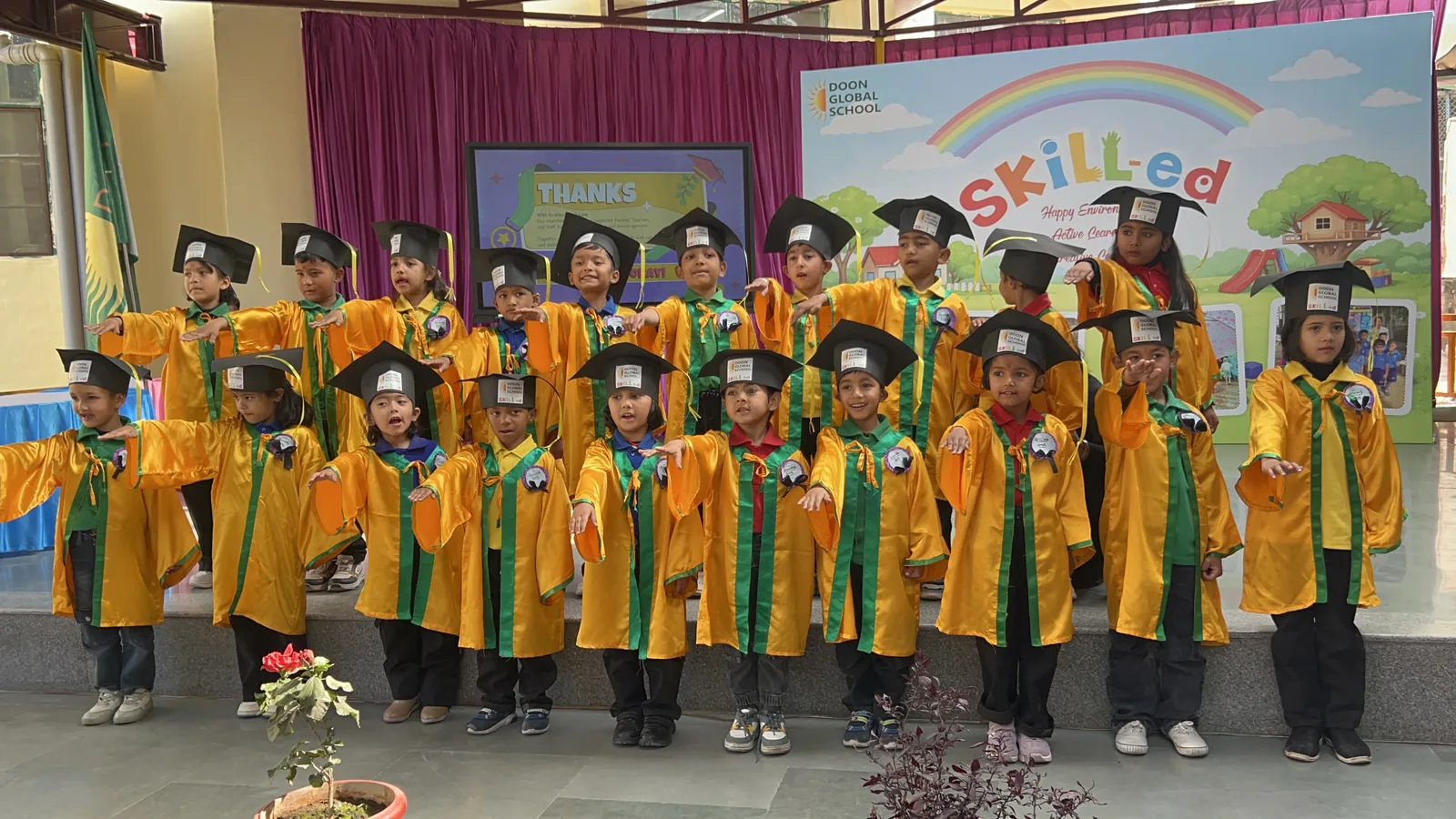 Kindergarten students in yellow graduation gowns and caps standing together on stage