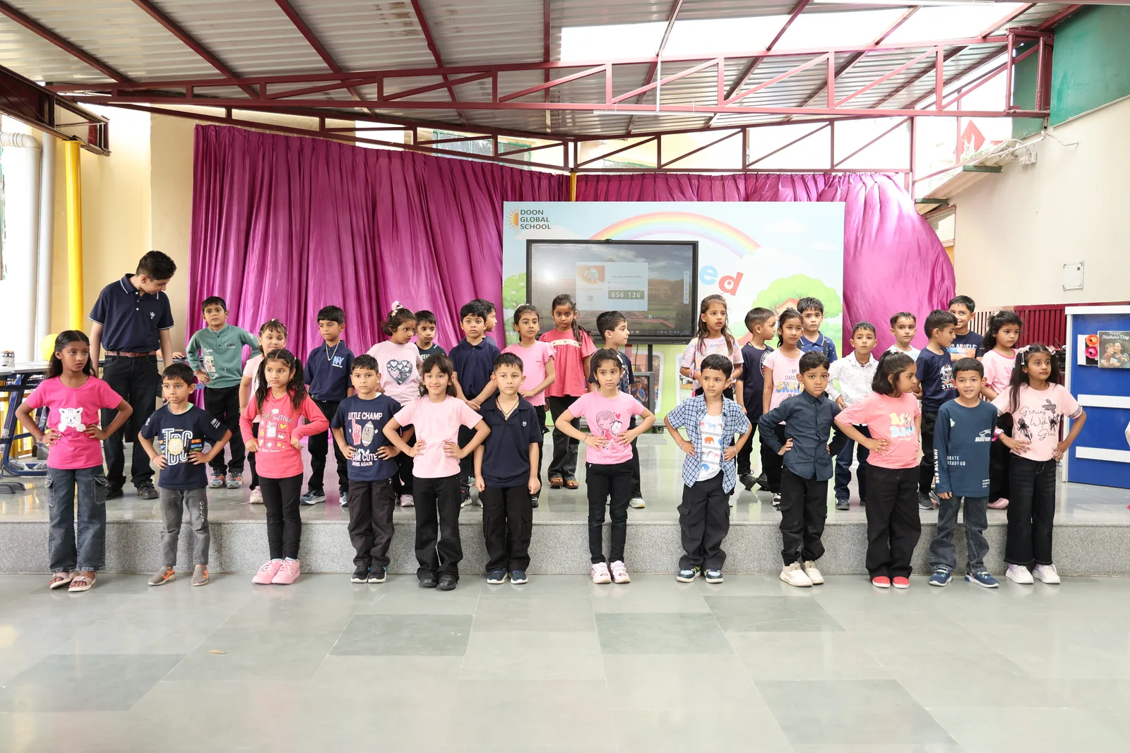 Pre-primary students lined up on stage in pink and black outfits during a school programme