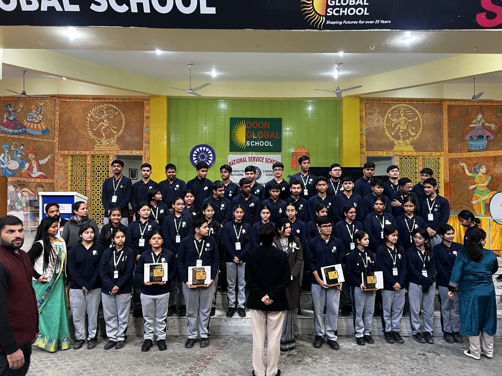 Students holding certificates in a group photograph with staff at the school entrance on Republic Day
