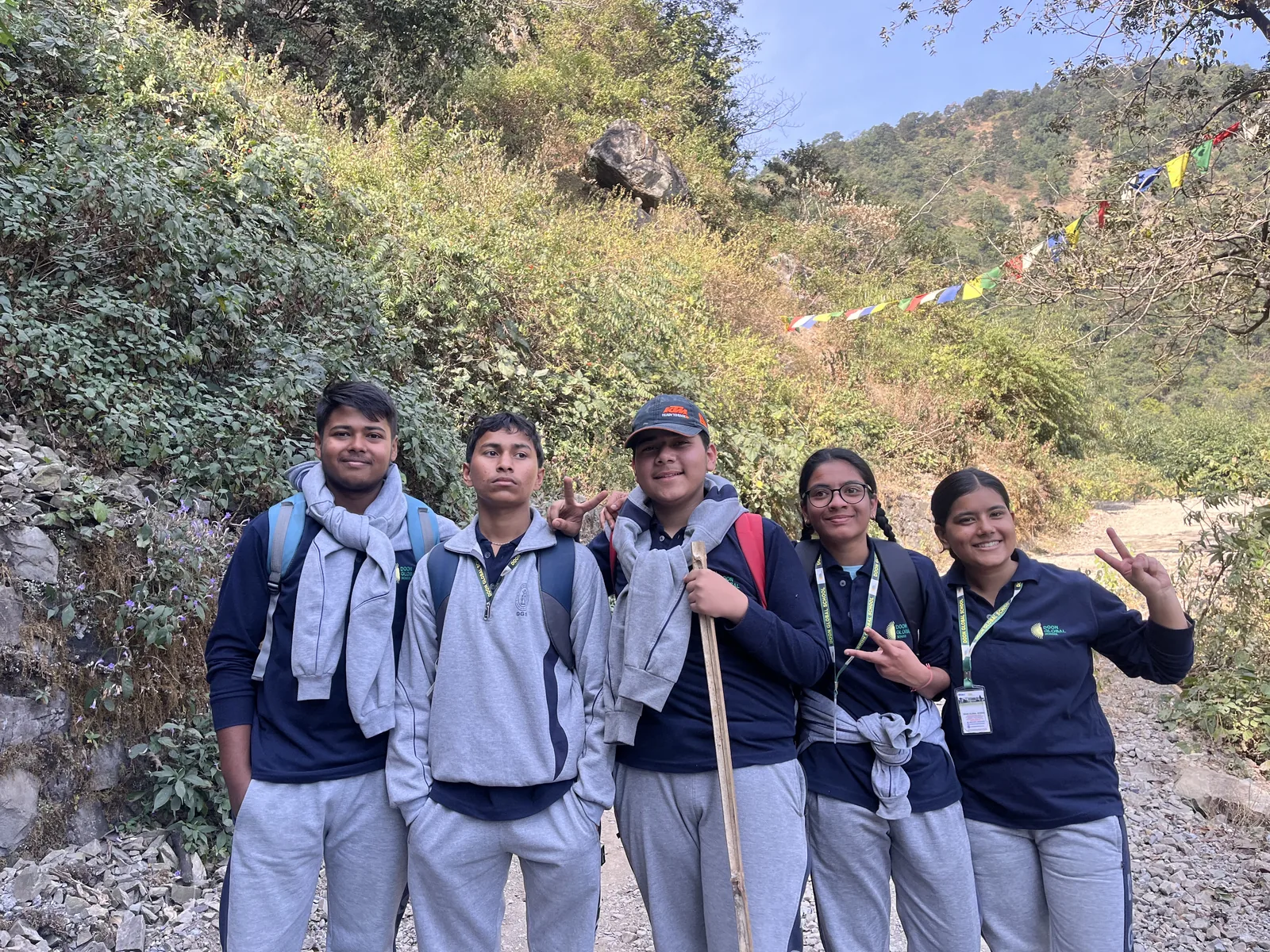 Students with walking sticks on a hill trail lined with prayer flags during the school trek