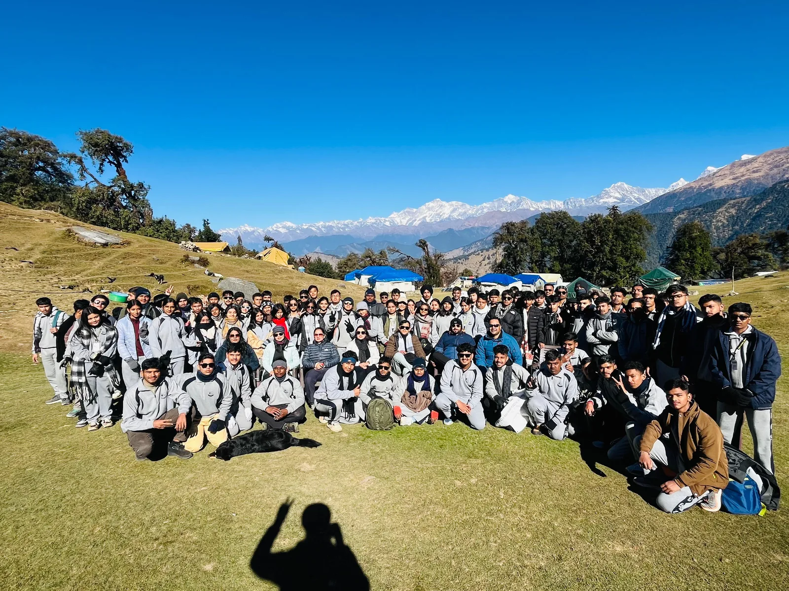 The whole group photographed on a meadow with snow-capped Himalayan peaks behind