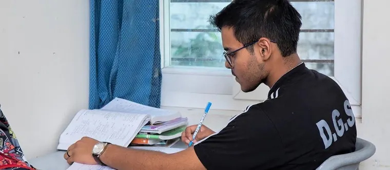A student studying at a desk with notebooks and a pen